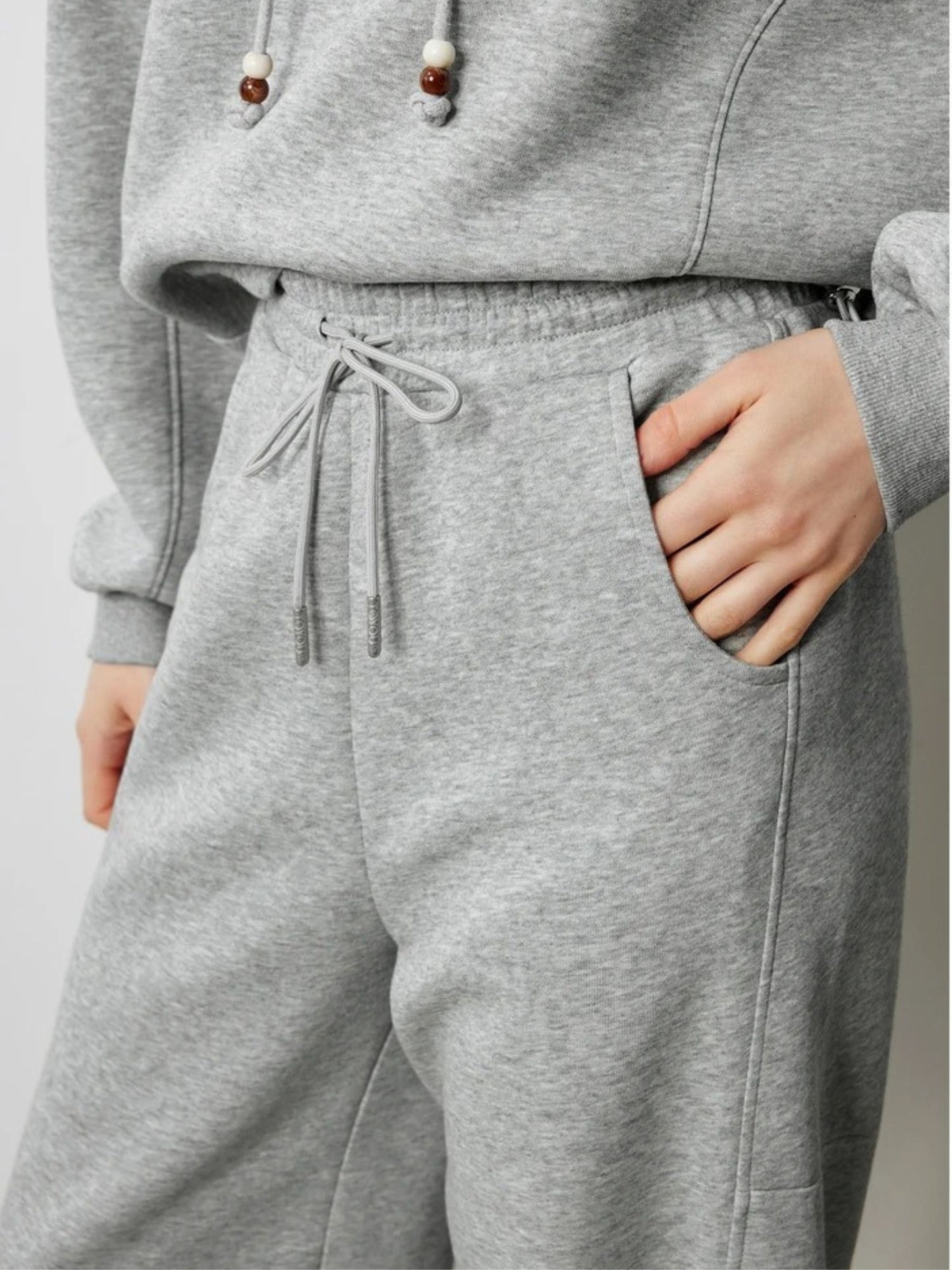 Close up of a young woman wearing a gray drawstring hoodie paired with gray drawstring high-waisted pants