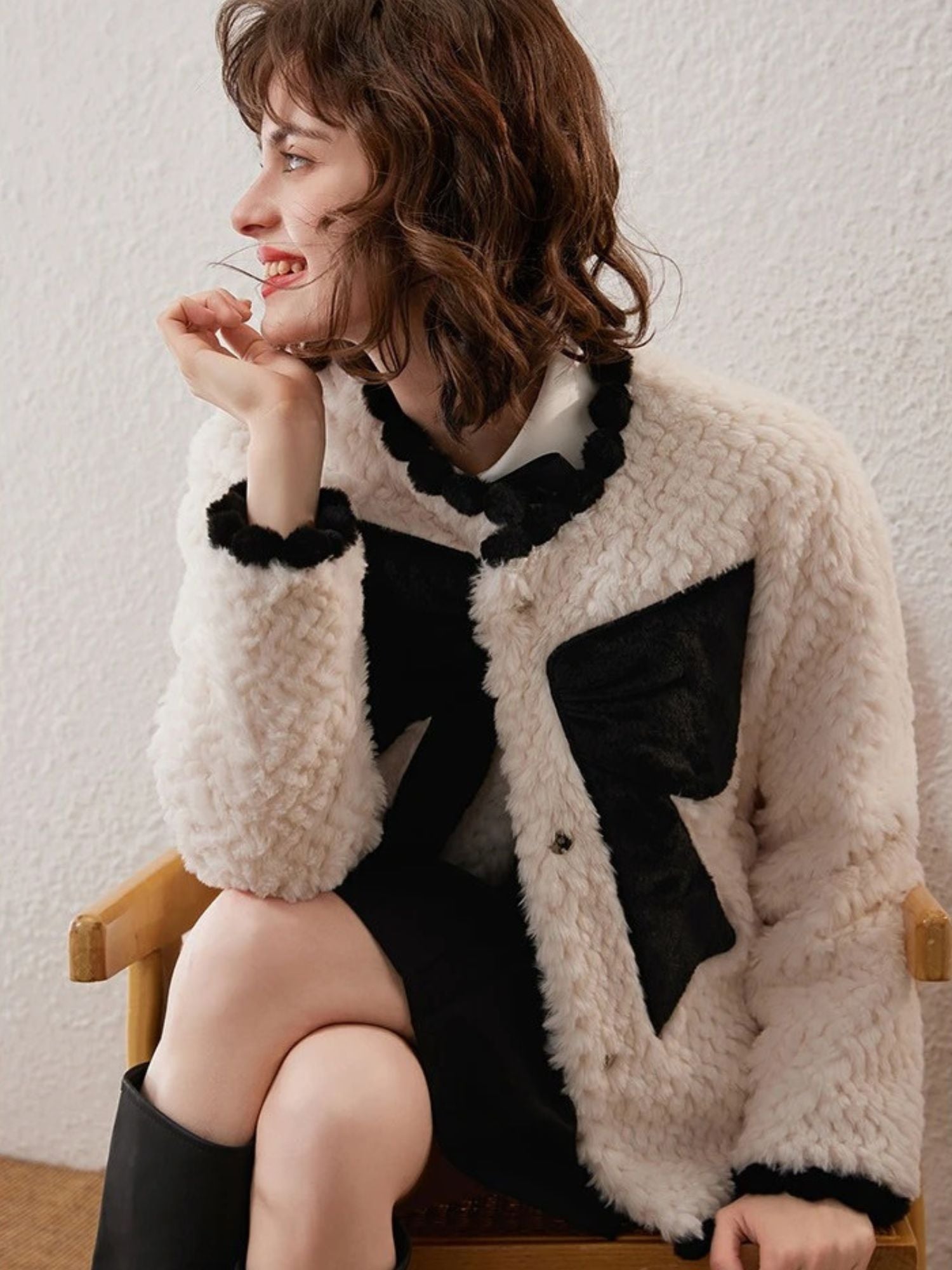 Woman in white cardigan with black bows, seated with hand on chin, smiling