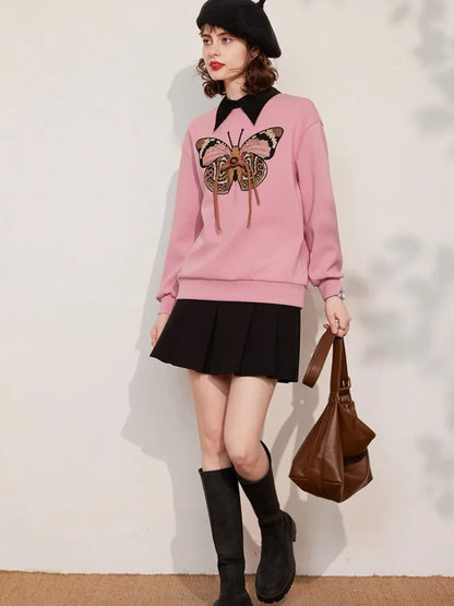 Full-body view of woman in pink embroidered sweatshirt, black skirt, and brown bag