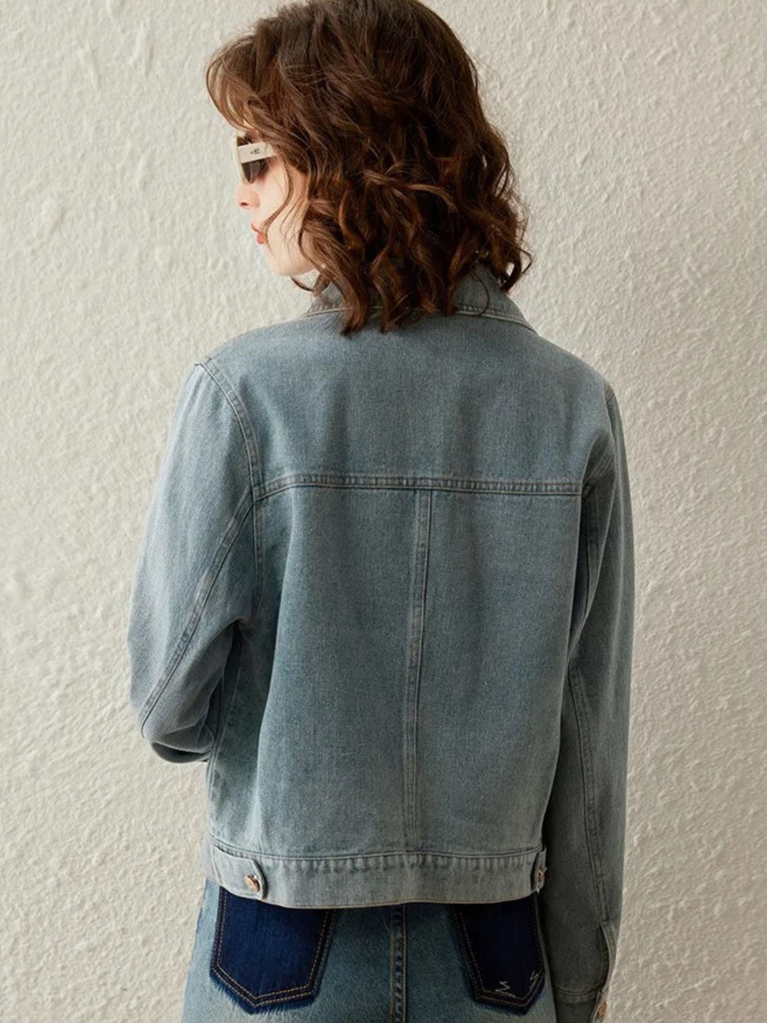Back view of woman in light blue denim jacket and jeans, with curly hair