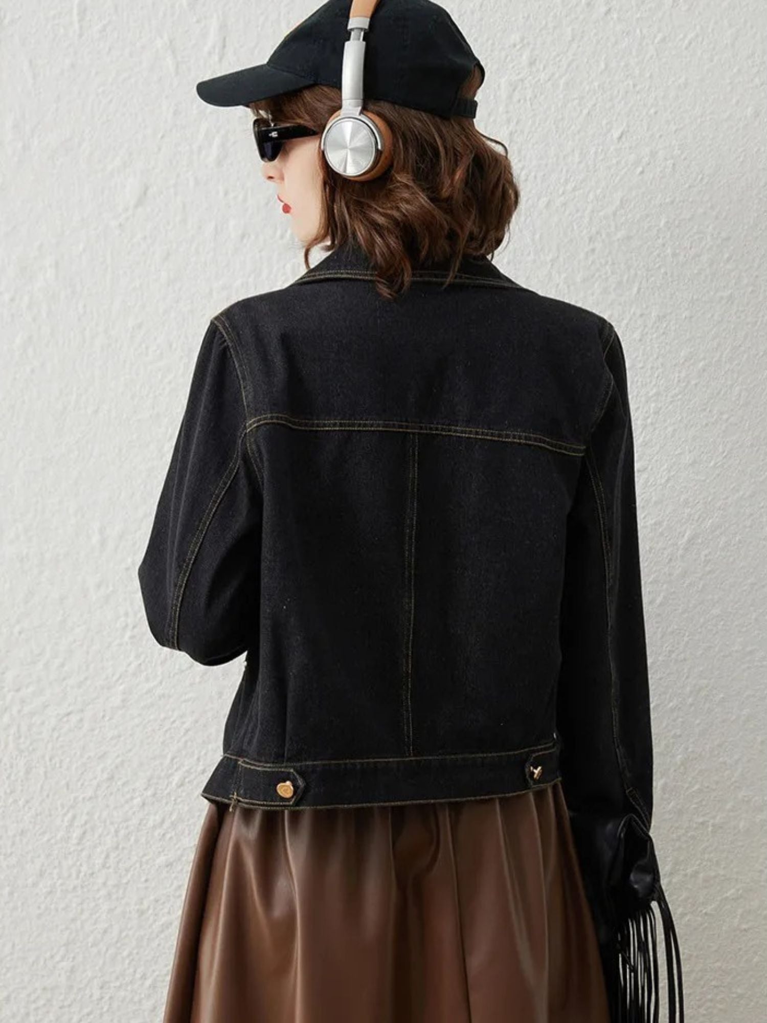 Back view of woman wearing black denim jacket with gold button details and brown skirt