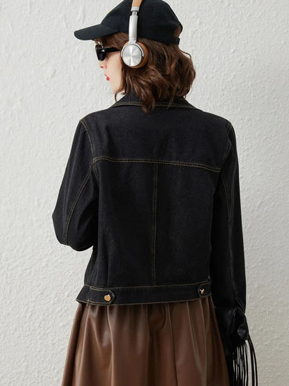 Back view of woman wearing black denim jacket with gold button details and brown skirt
