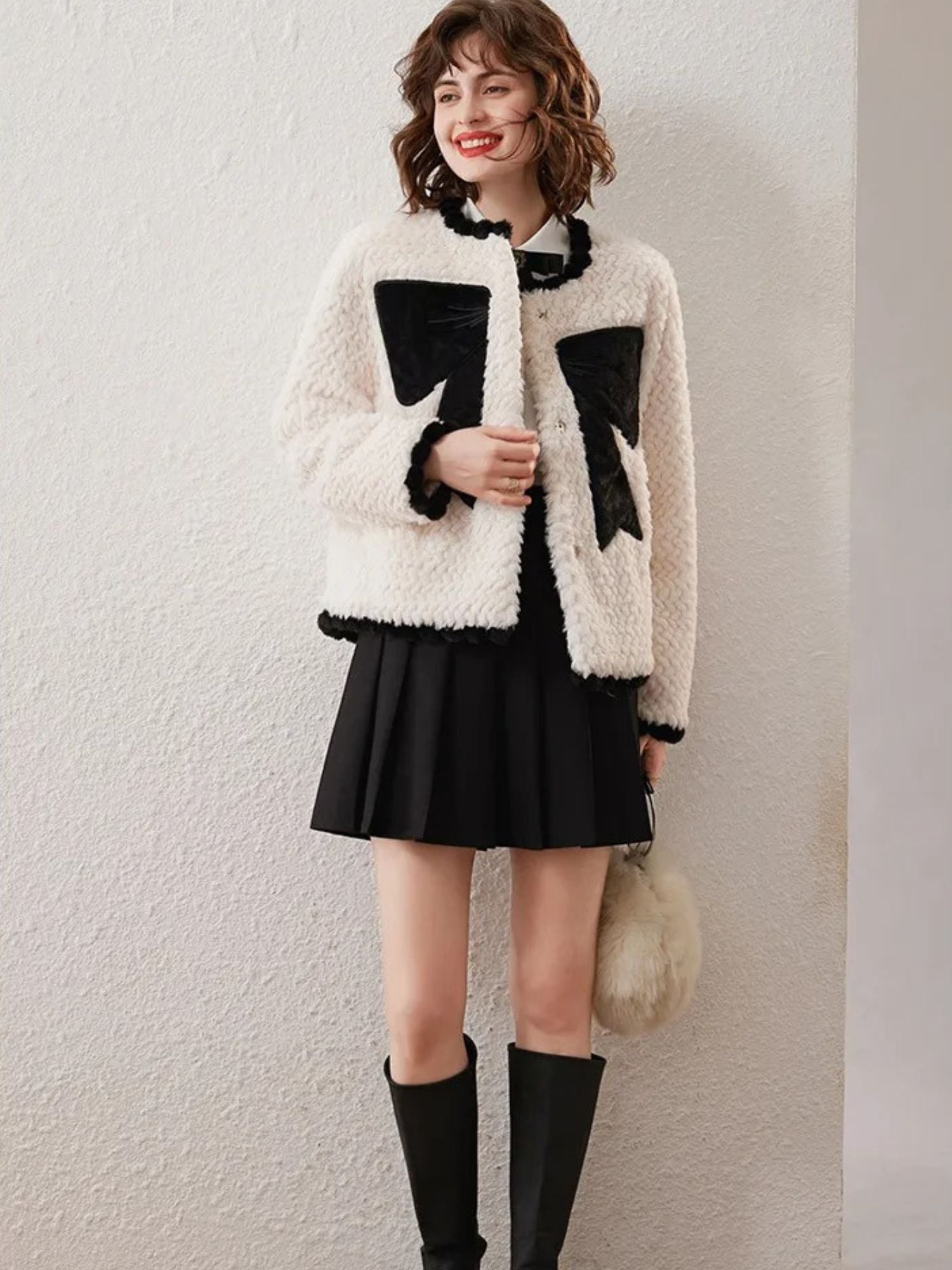 Woman in white cardigan with black bows, standing with black skirt and knee-high boots