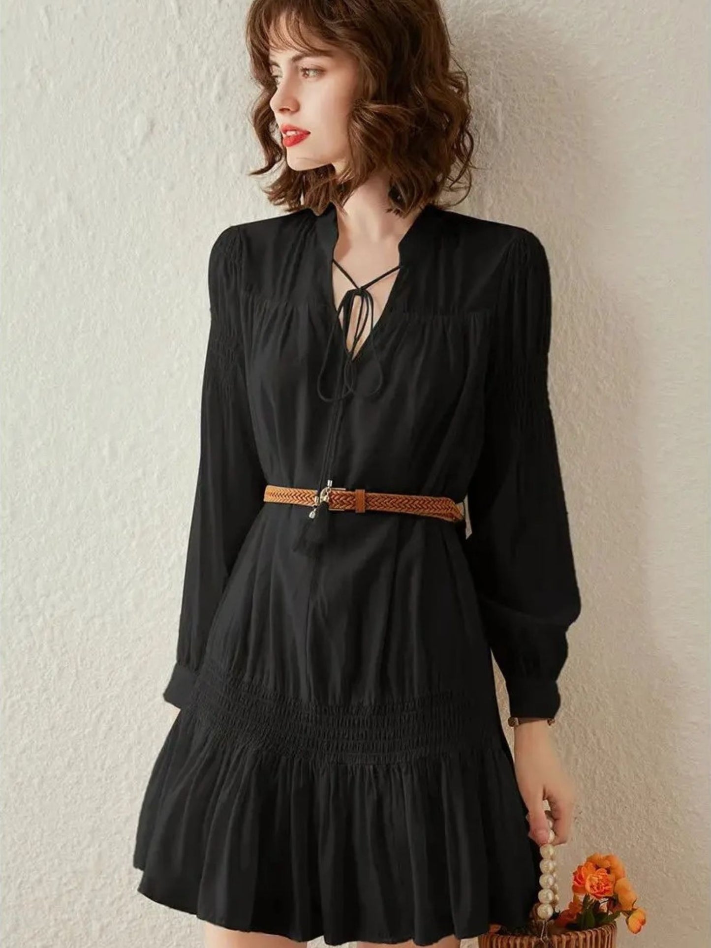 Woman in black pleated mini dress with brown belt and hat, posing with fringe bag