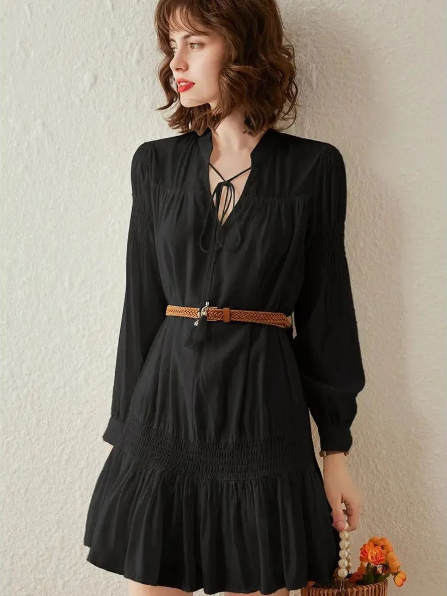 Woman in black pleated mini dress with brown belt and hat, posing with fringe bag