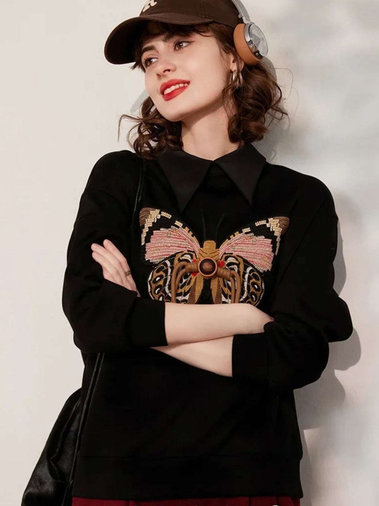 Woman wearing black sweatshirt with butterfly embroidery, styled with black skirt and cap