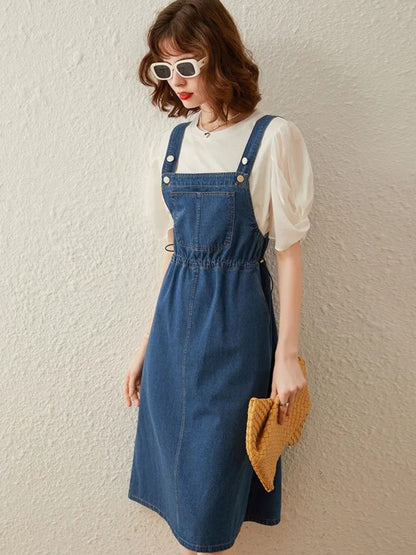 Full-body view of denim overall dress with puff-sleeve blouse and yellow clutch