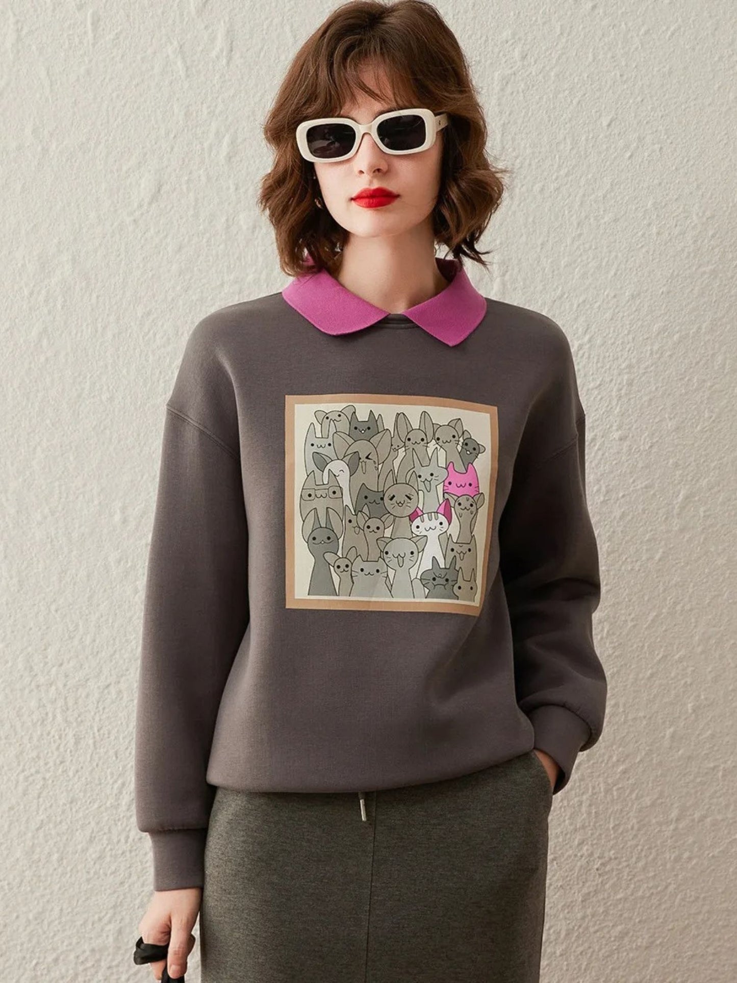 Woman wearing a grey sweatshirt with graphic print on the front, styled with a pink collared shirt and pencil skirt