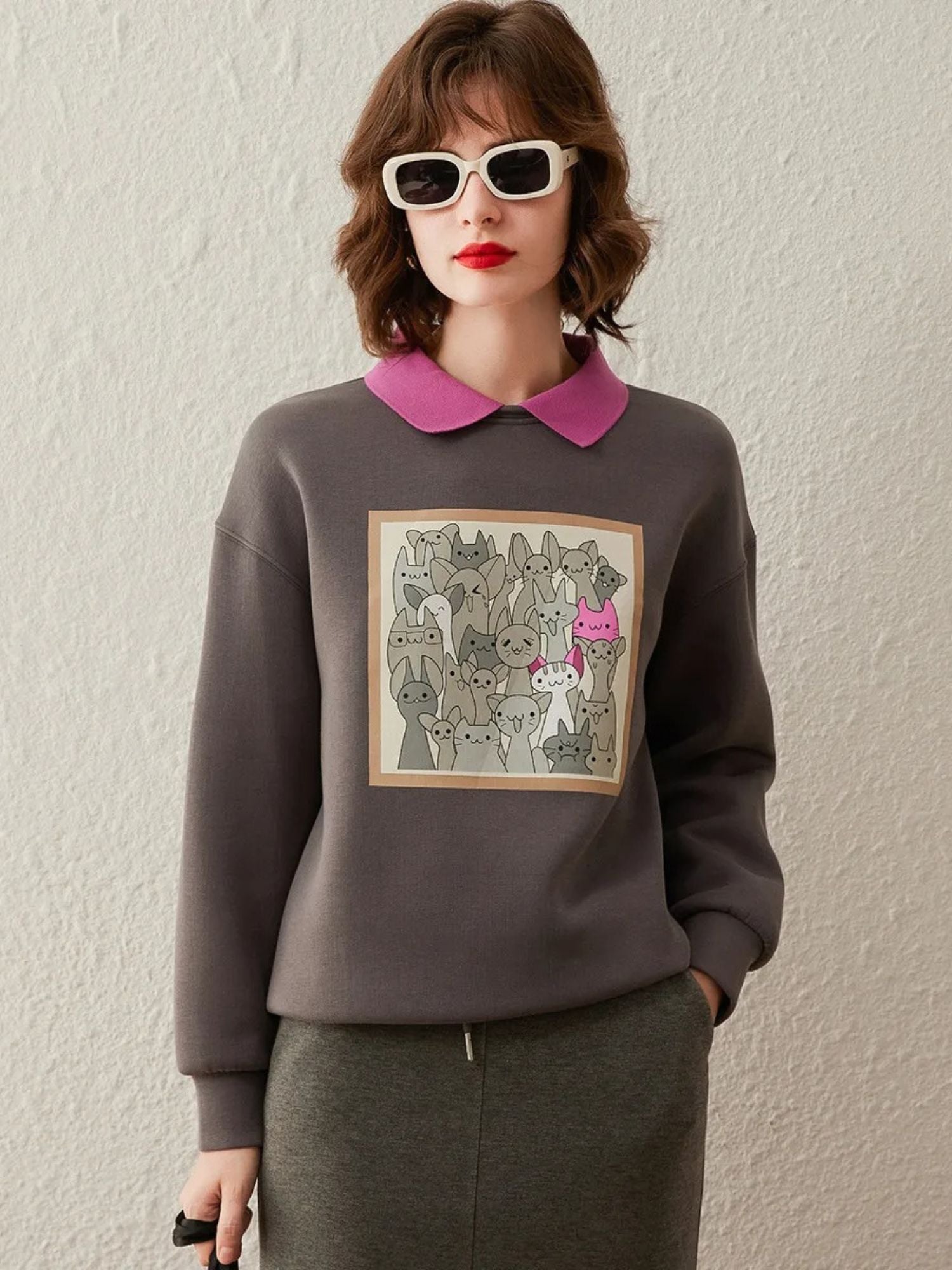 Woman wearing a grey sweatshirt with graphic print on the front, styled with a pink collared shirt and pencil skirt