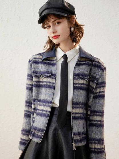 Woman wearing a blue and white plaid jacket over a white shirt and black tie, paired with a black leather skirt and cap