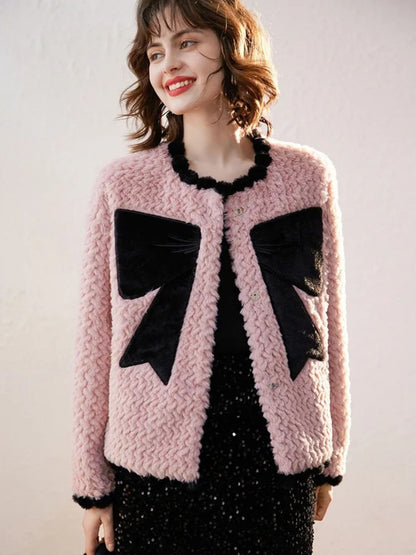 Woman wearing a pink textured cardigan with large black bow designs, smiling against a plain background
