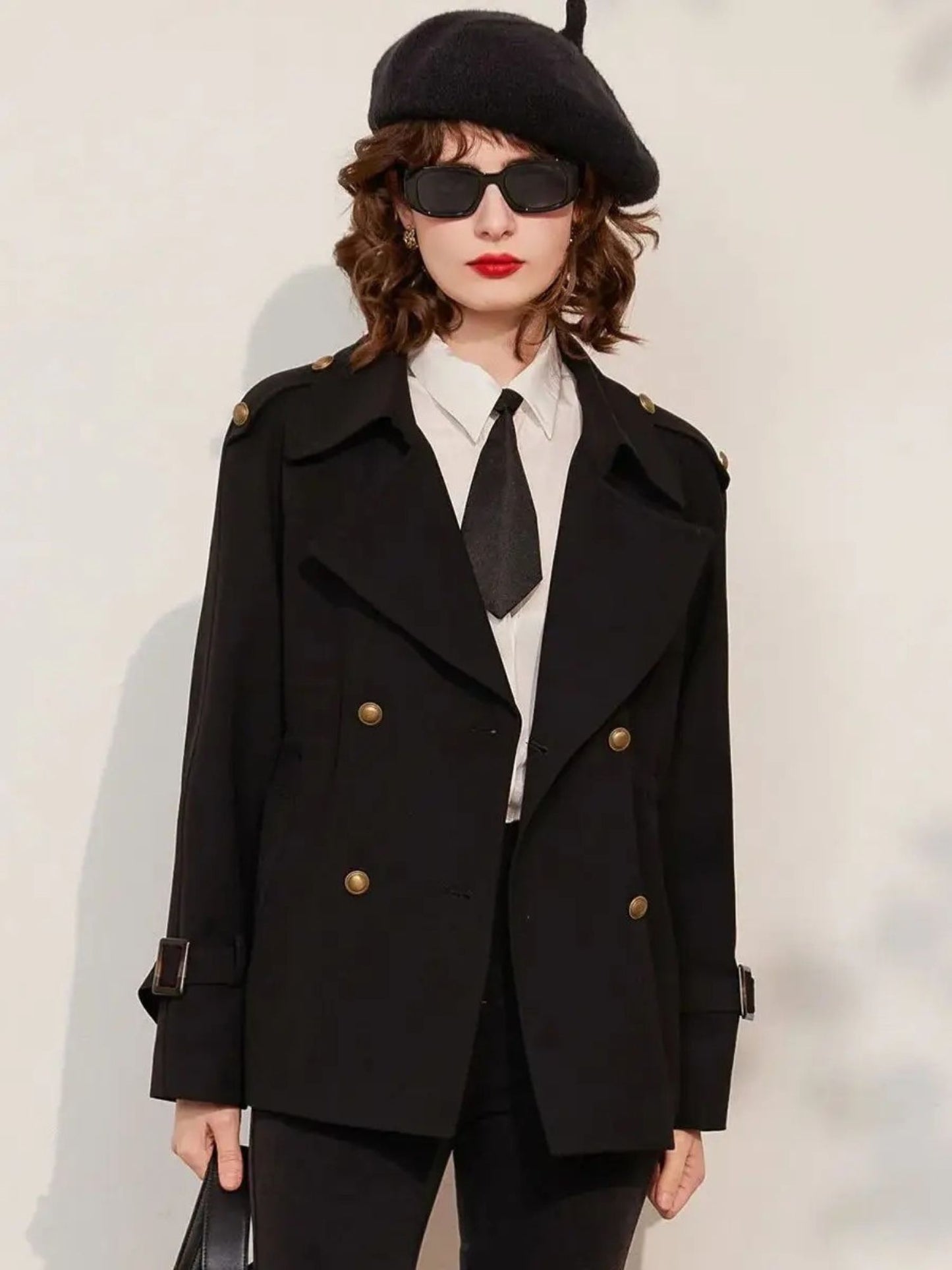 Full-body view of woman in black blazer and trousers, white shirt with tie, and beret, posing with hands in pockets