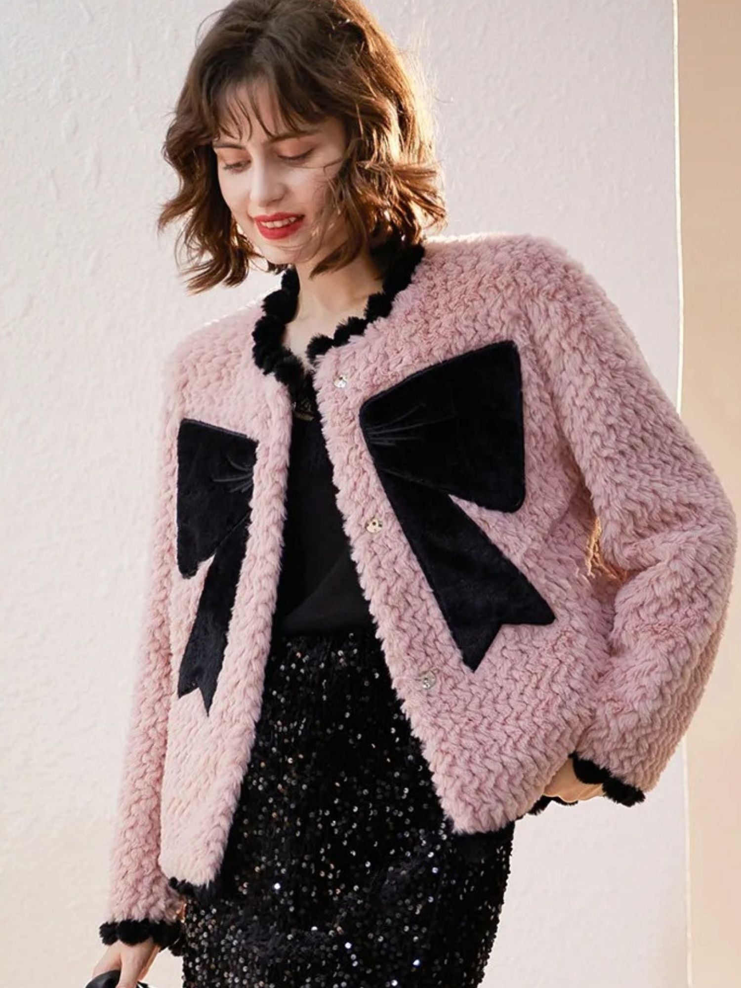 Side view of woman in pink cardigan with black bows, posing with one hand in pocket