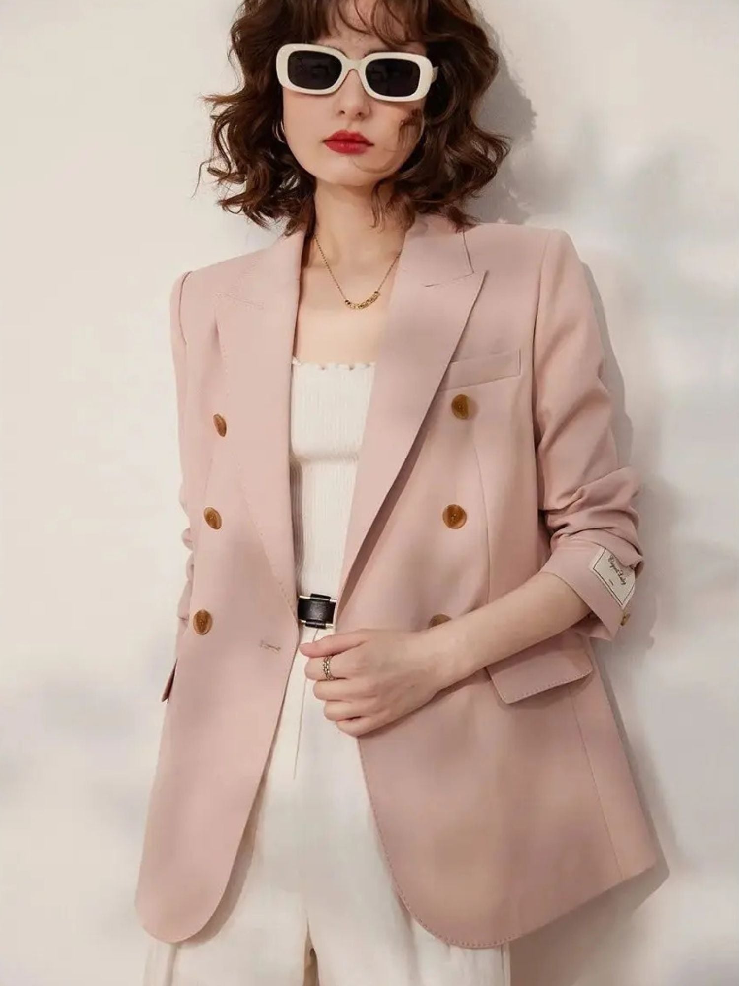 Front view of the woman wearing the pink blazer and white outfit, both hands in blazer pockets, showcasing the full upper body and accessories