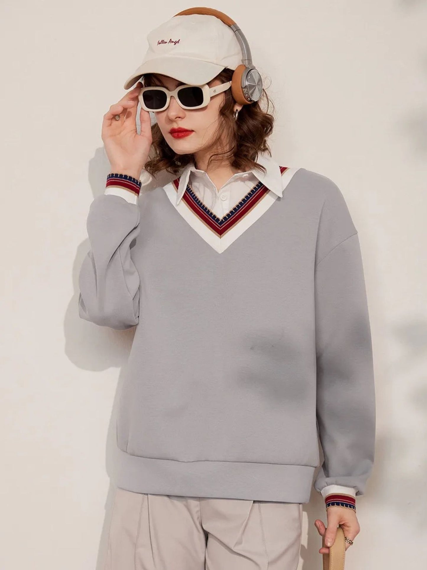 Full-body view of light grey V-neck sweatshirt with striped collar, paired with beige shorts and cap