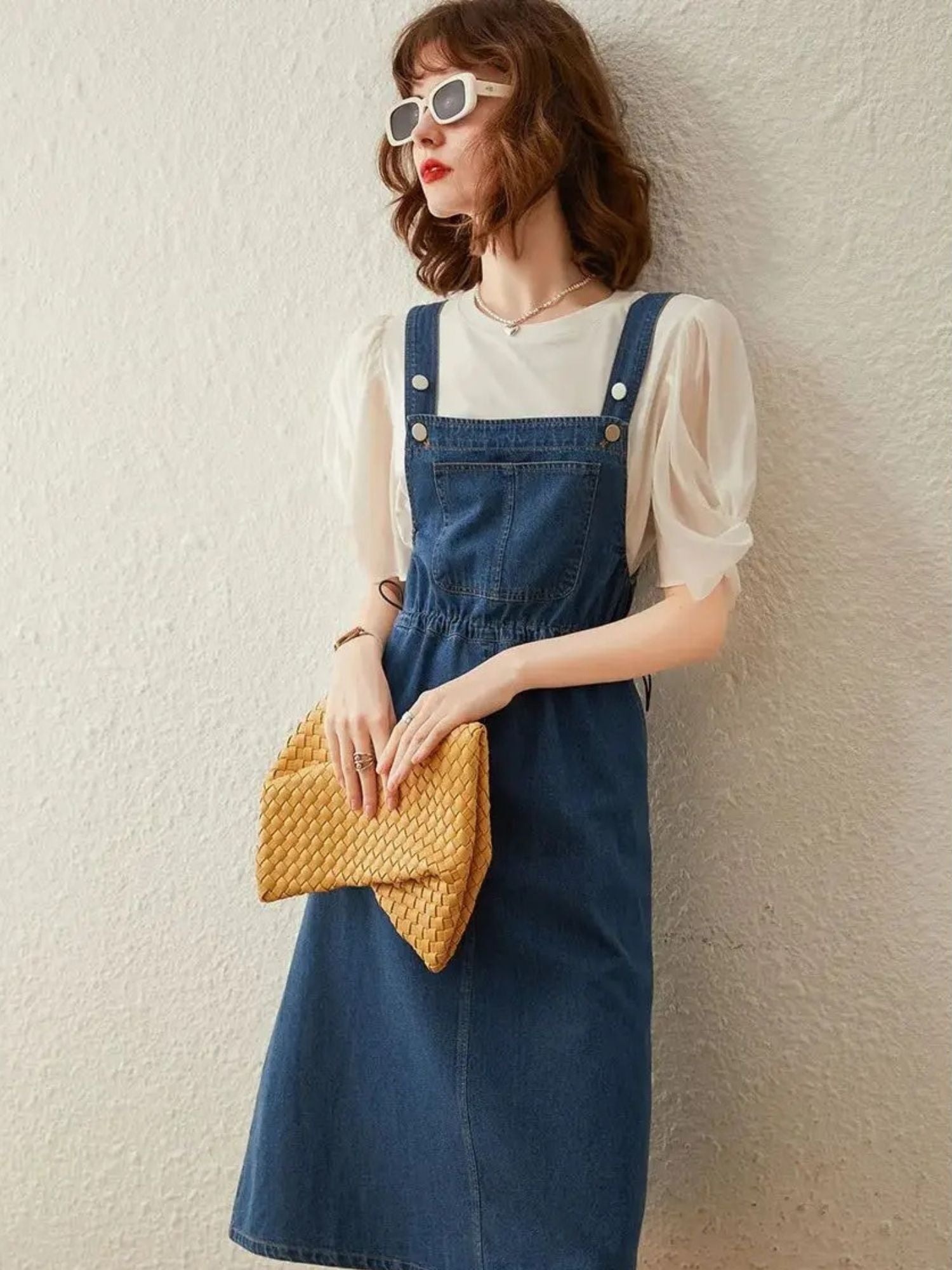 Woman posing in denim overall dress, hands on clutch