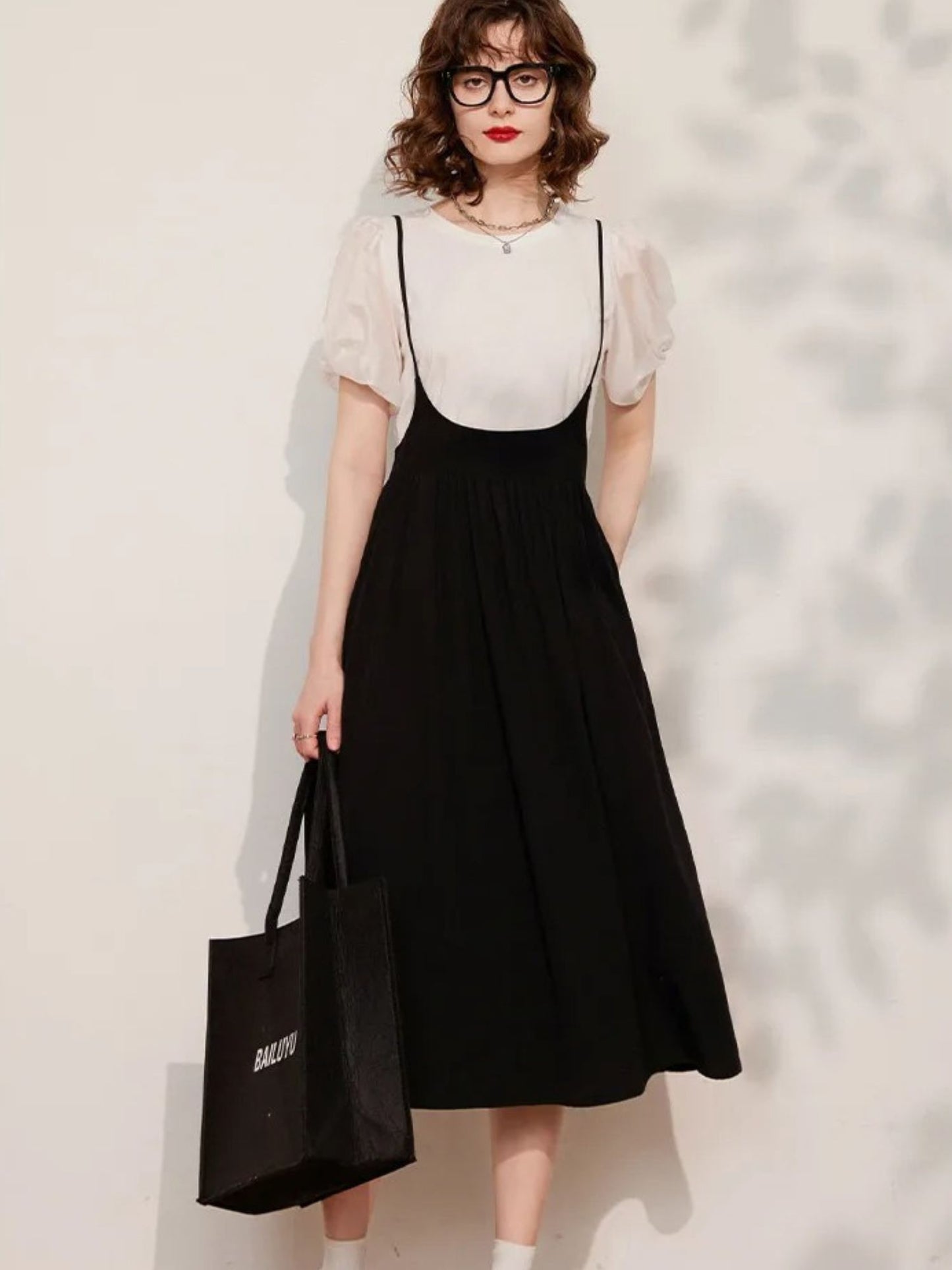 Woman wearing cream puff-sleeve blouse tucked into black midi skirt, holding black handbag