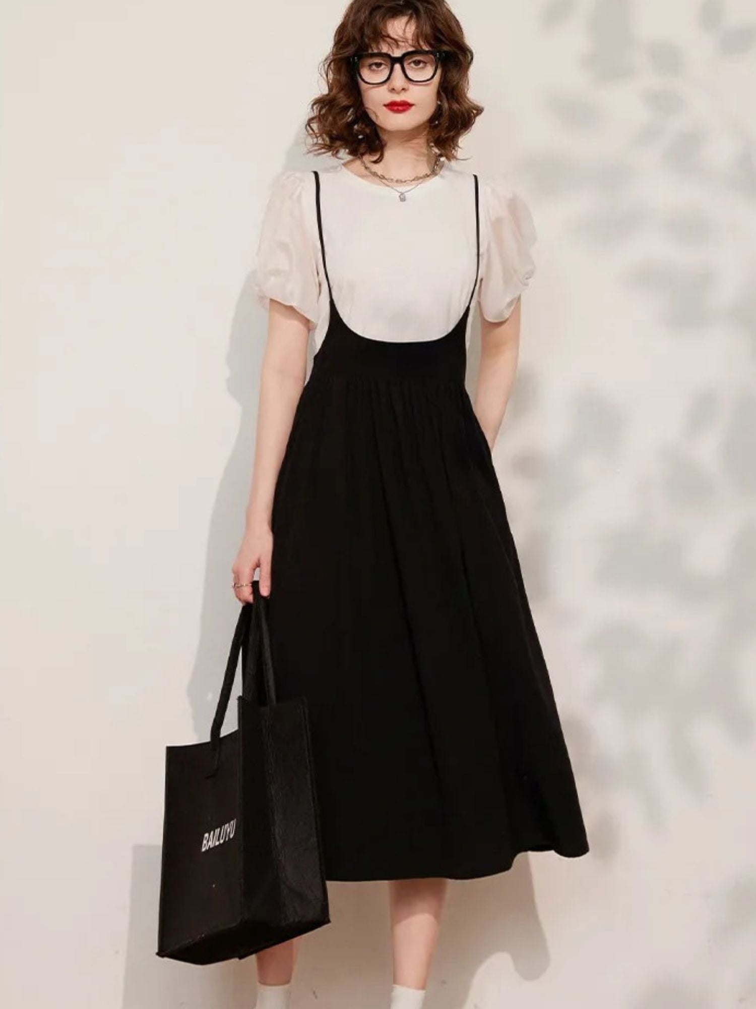 Woman wearing cream puff-sleeve blouse tucked into black midi skirt, holding black handbag