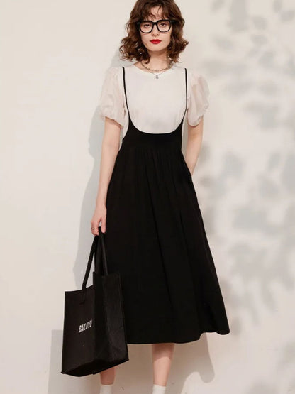 Woman wearing cream puff-sleeve blouse tucked into black midi skirt, holding black handbag