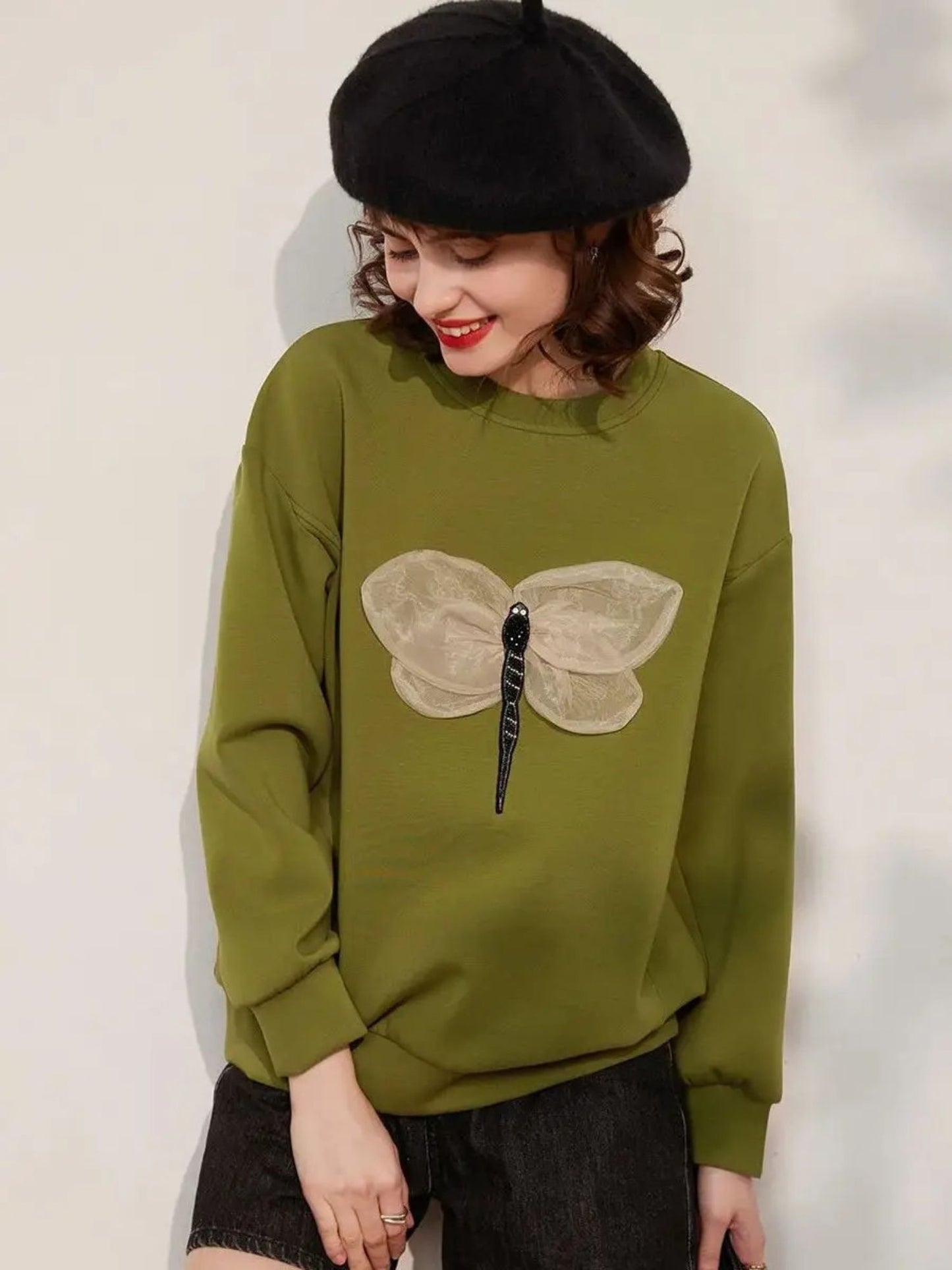 Woman wearing a green sweatshirt with large butterfly embroidery, styled with black skirt and beret