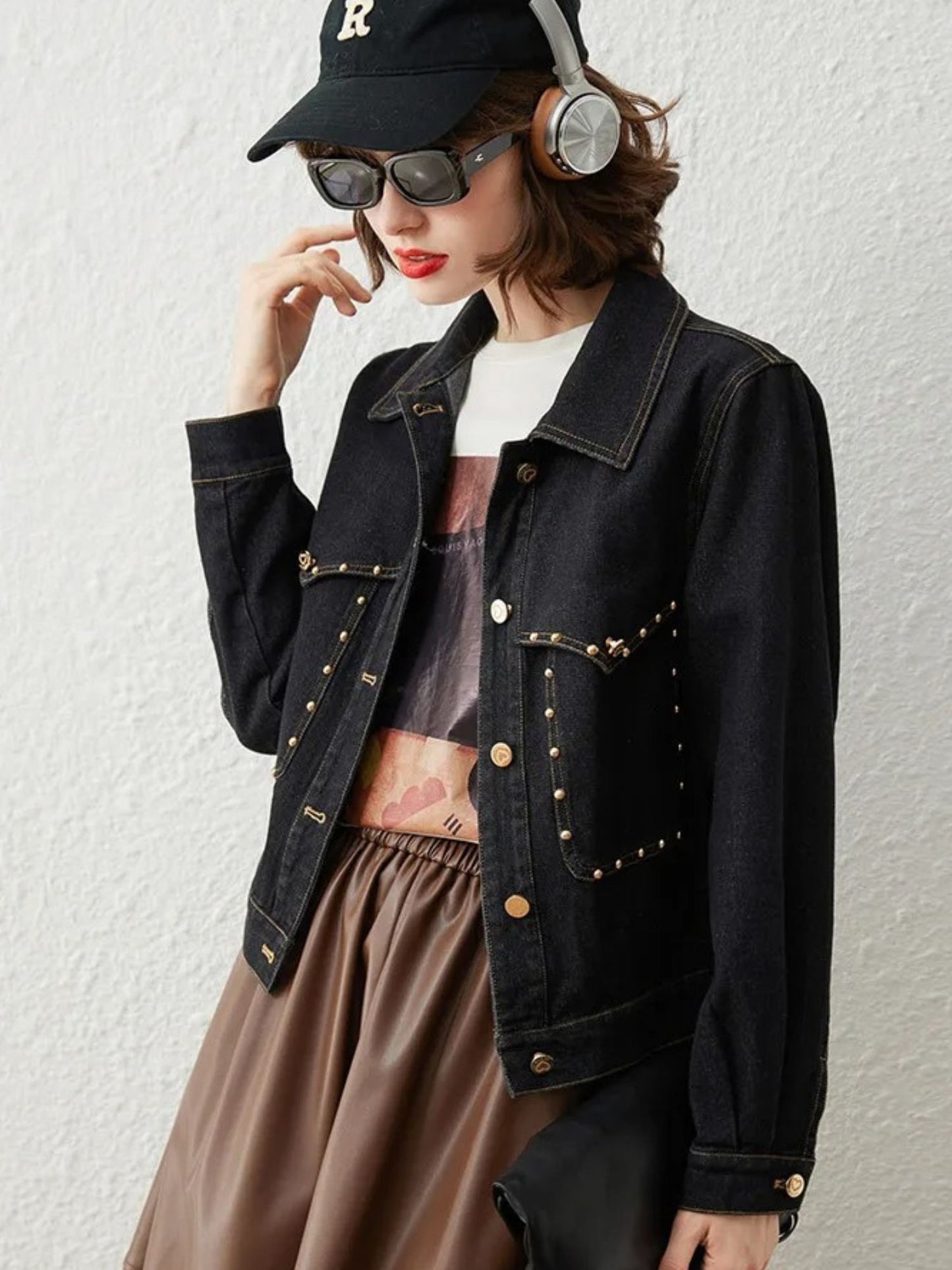 Side view of woman in black denim jacket with gold button details, brown skirt, and cap