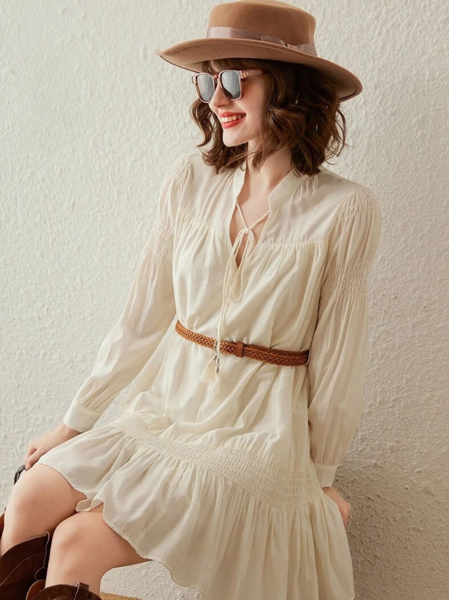 A woman wearing a boho-style long sleevve dress with a tie detail in the neckline and a brown belt