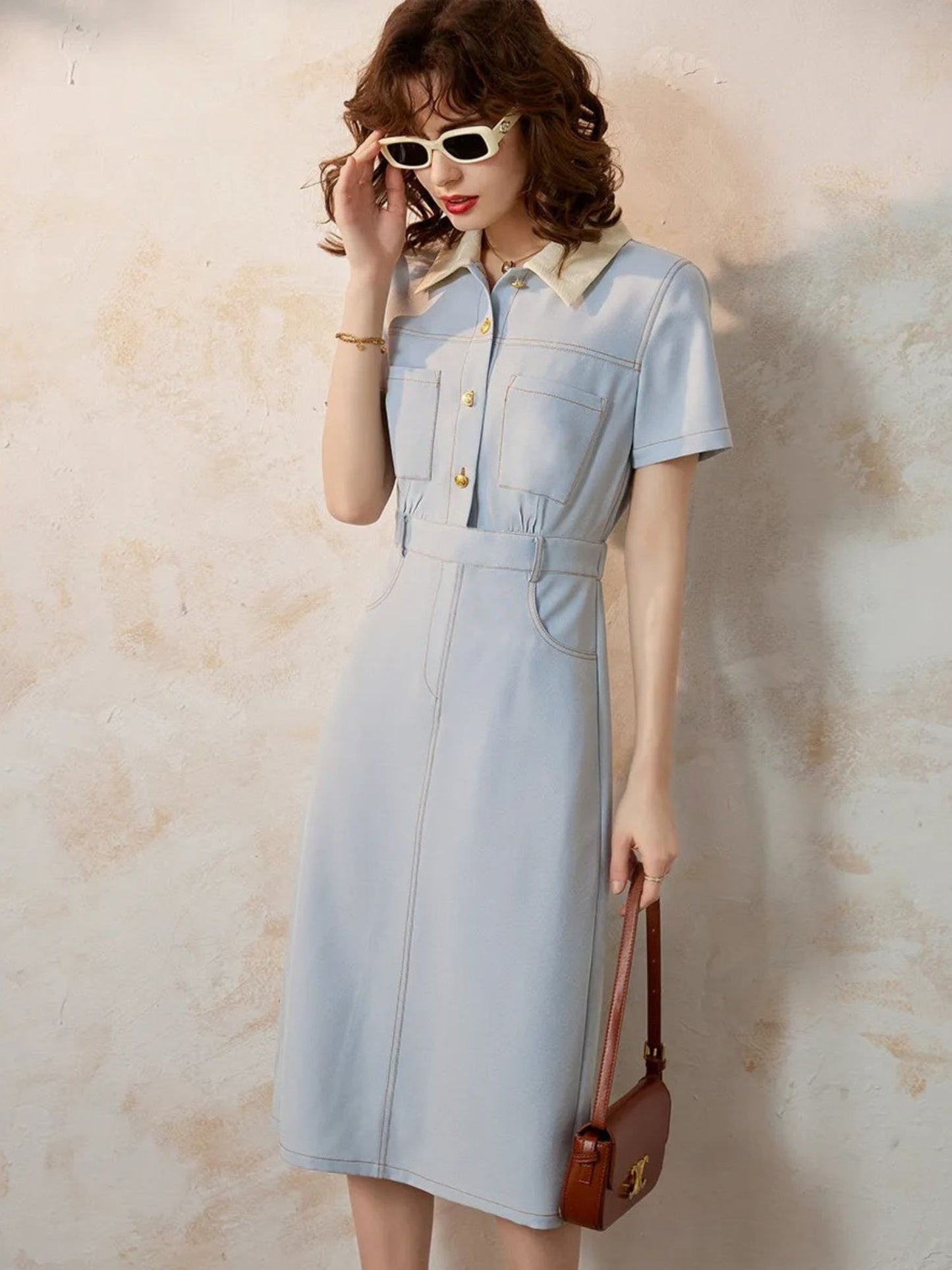 Woman posing in light blue collared dress holding handbag