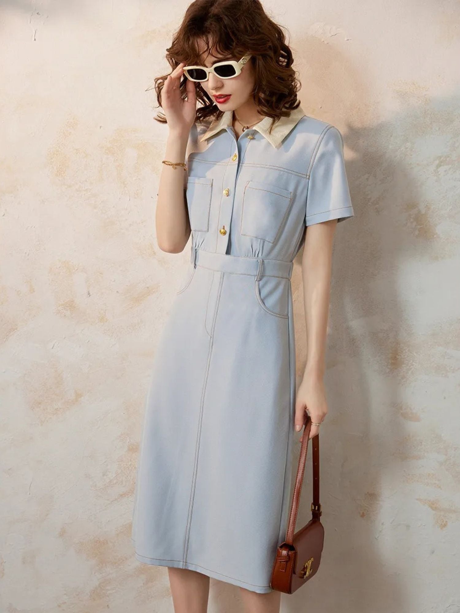 Woman posing in light blue collared dress holding handbag