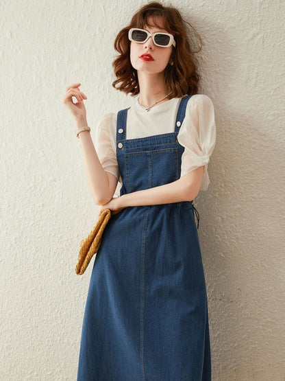Woman wearing cream puff-sleeve blouse with denim overall dress, holding yellow clutch