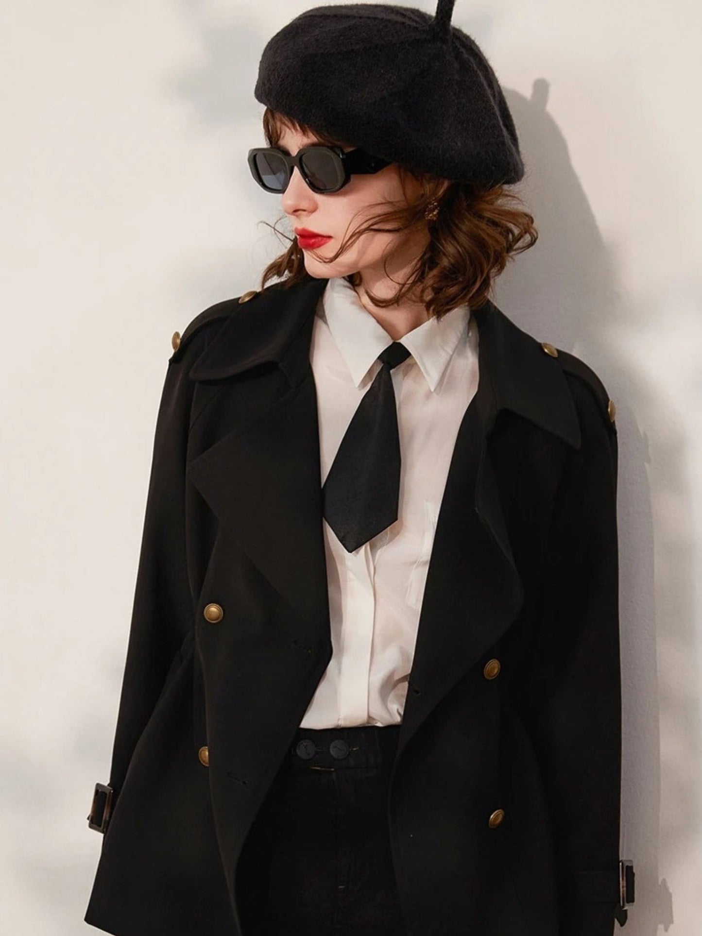 Front view of woman in black blazer with gold buttons, styled with white shirt, tie, and beret