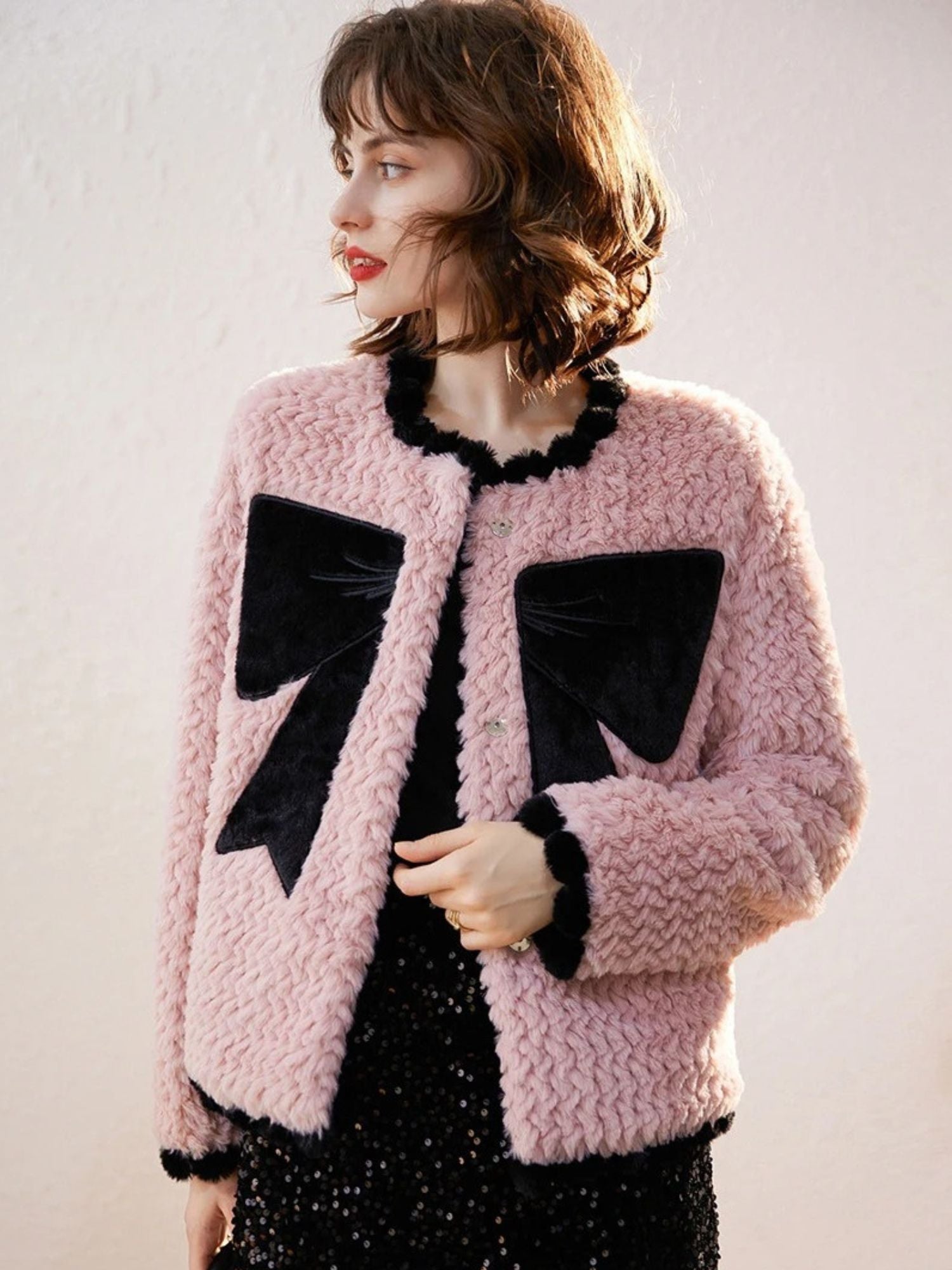 Woman wearing pink cardigan with black bows, facing forward with relaxed pose