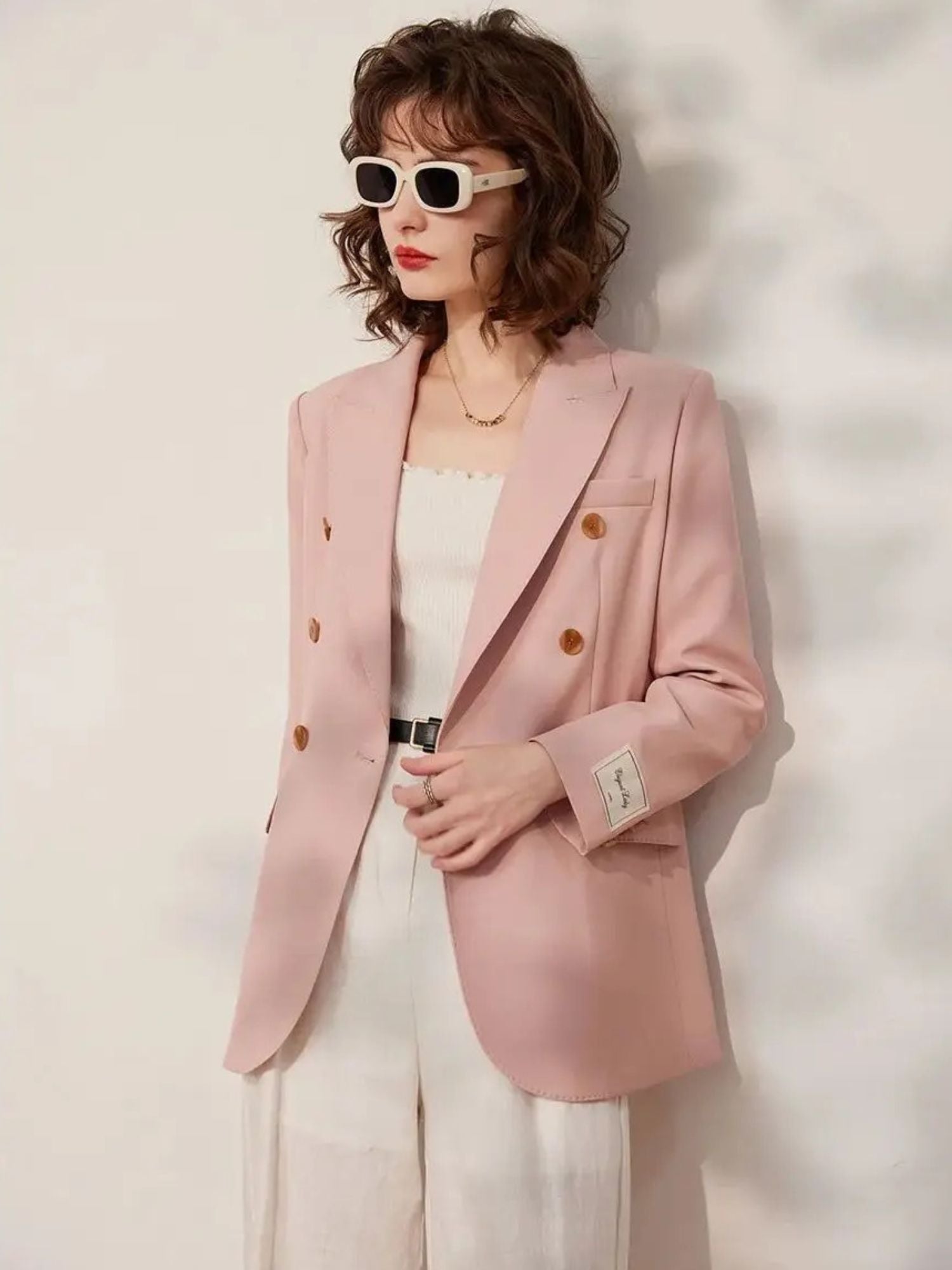 Three-quarter angle view of the woman turned slightly to her right, with one hand in the blazer pocket, emphasizing the tailored fit and button details