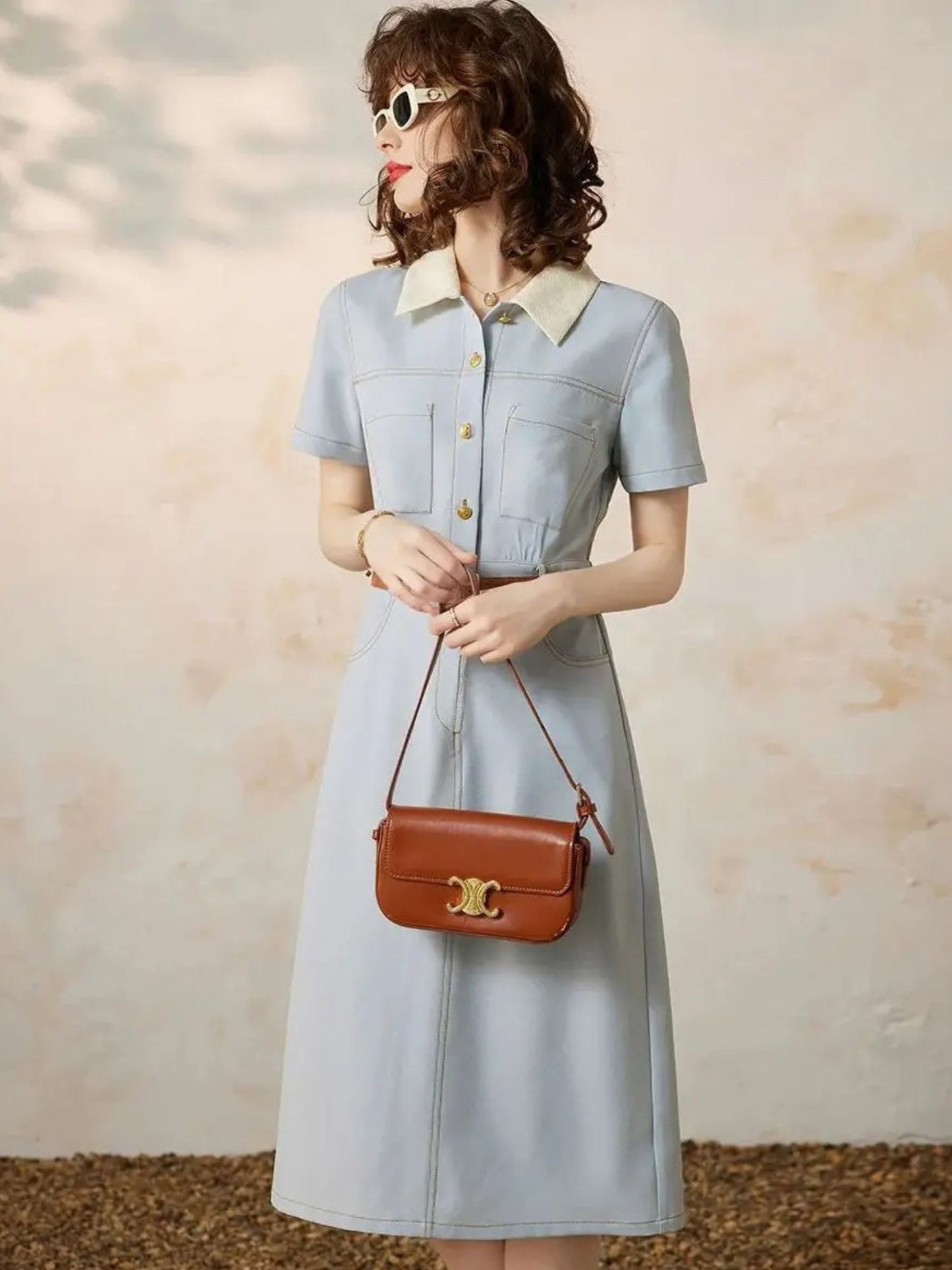 A woman wearing a light blue A-line shirt dress with a turn-down collar, button-through front, and short sleeves
