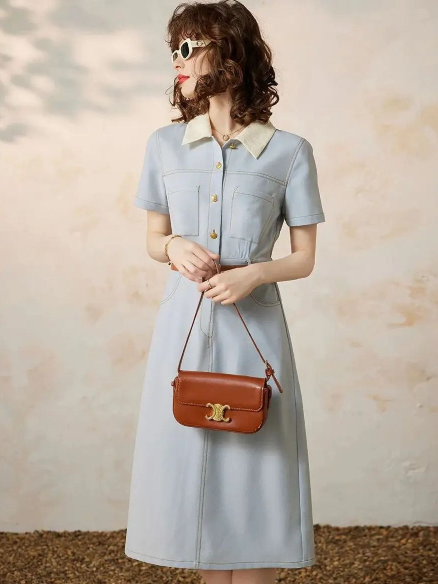 A woman wearing a light blue A-line shirt dress with a turn-down collar, button-through front, and short sleeves
