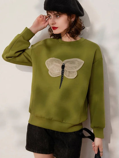 Woman posing in green embroidered sweatshirt with black skirt, hand raised to head