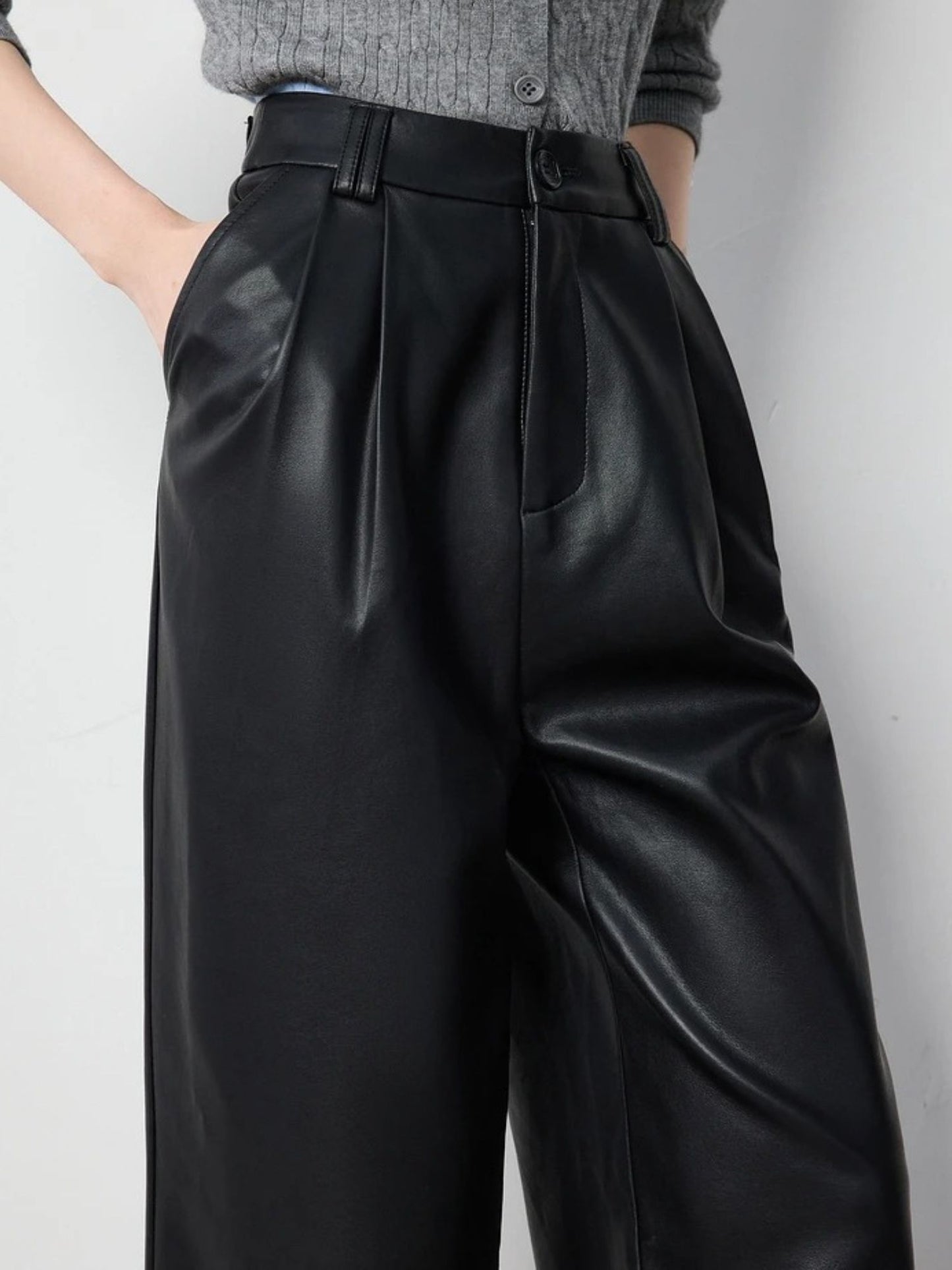 Close-up front view of black faux leather pants with pleated detail and side pockets