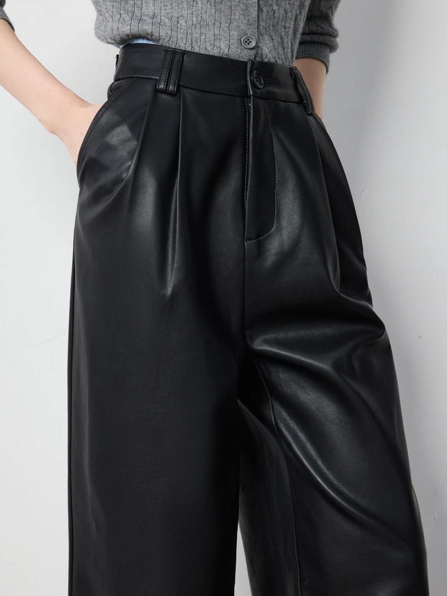 Close-up front view of black faux leather pants with pleated detail and side pockets