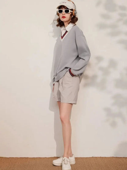 Woman in grey striped collar sweatshirt and shorts, standing against wall