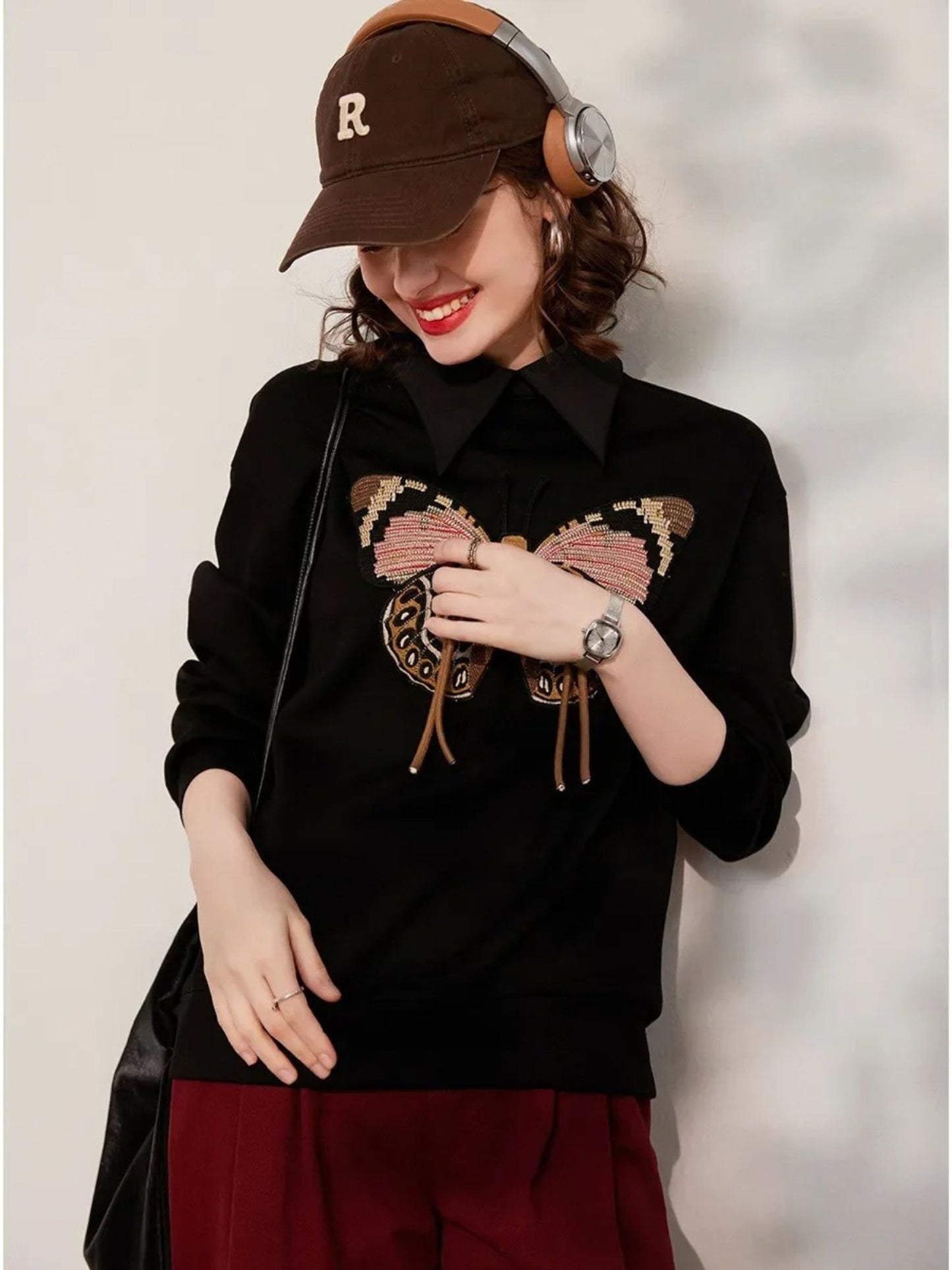 Side view of black embroidered sweatshirt with butterfly design, styled with cap