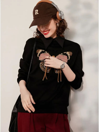 Side view of black embroidered sweatshirt with butterfly design, styled with cap
