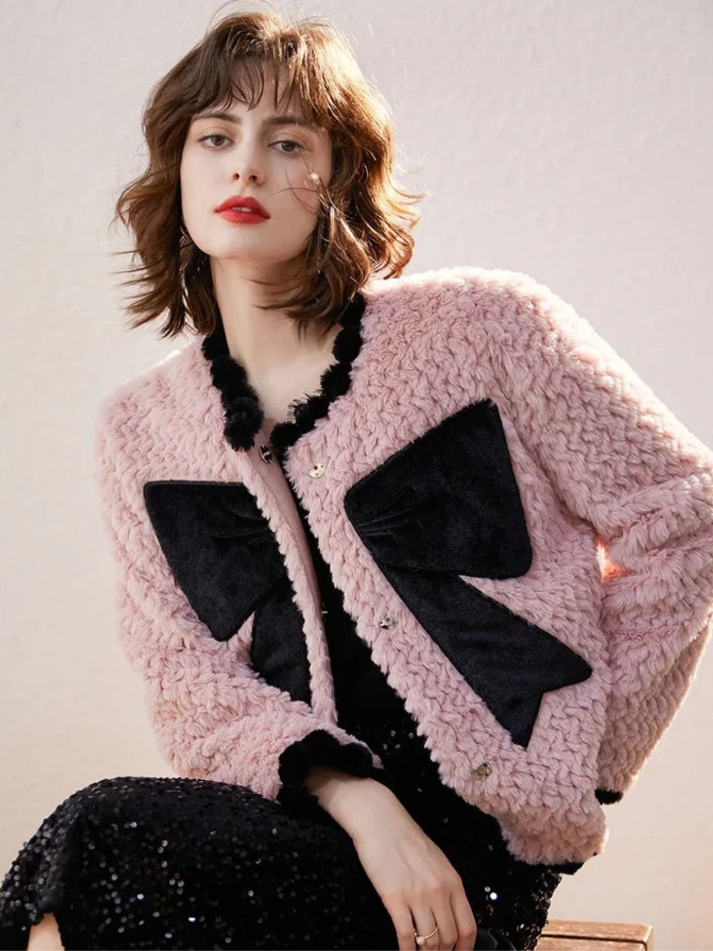 Woman in pink cardigan with black bows, standing with slight angle, looking down