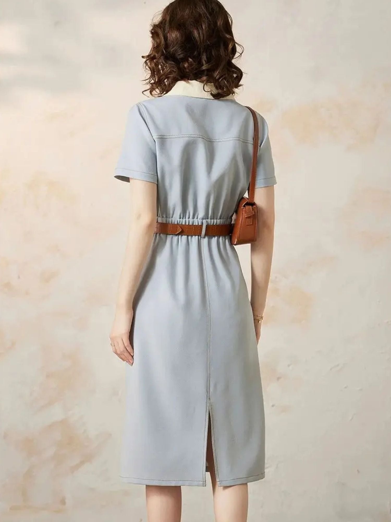 Back view of awoman wearing a light blue A-line shirt dress with a turn-down collar, button-through front, and short sleeves