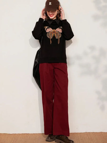Full body view of butterfly embroidery detail on sweatshirt, showing pink and gold tones