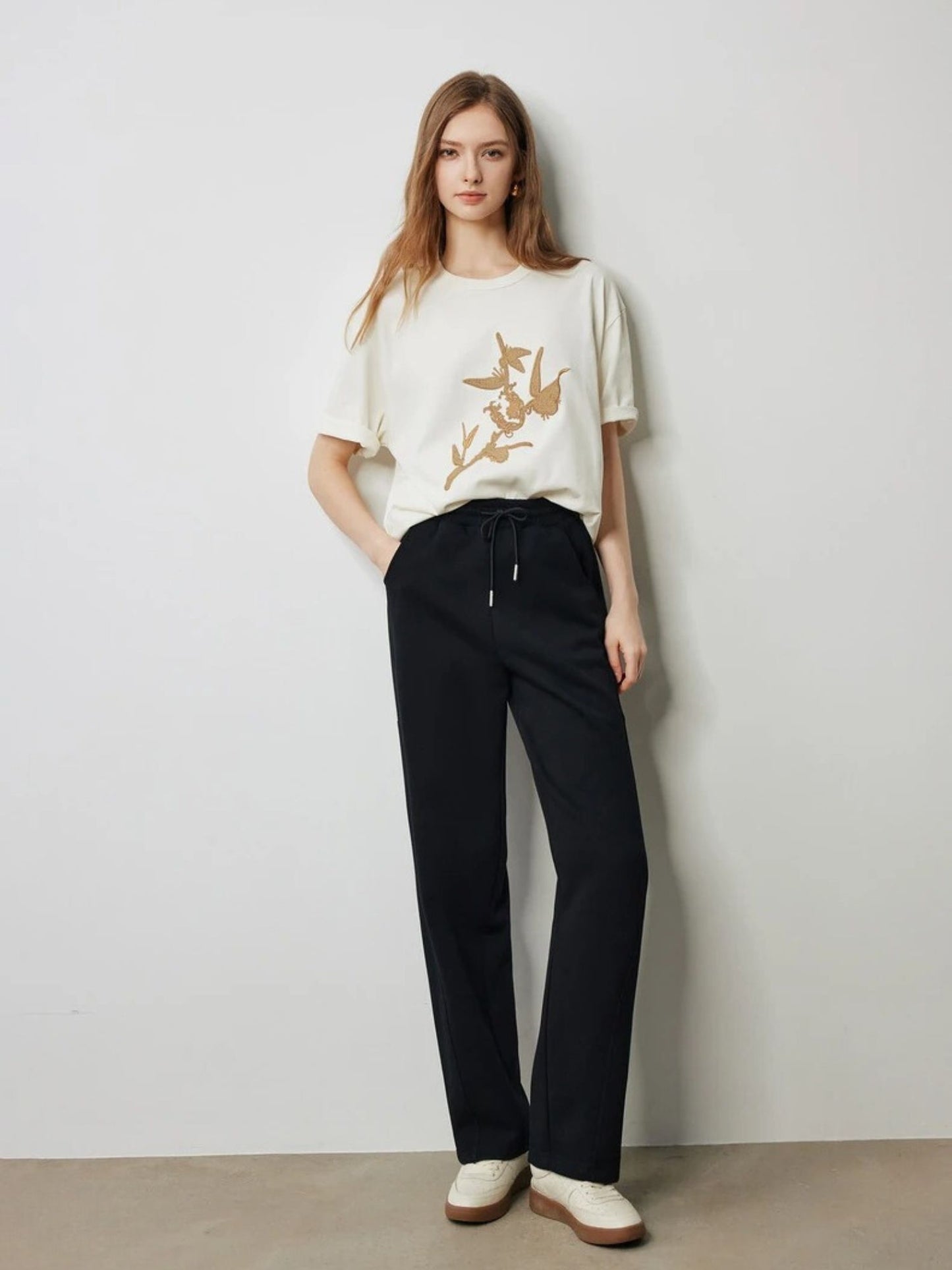 Full-body view of woman in black drawstring trousers with white t-shirt and flats