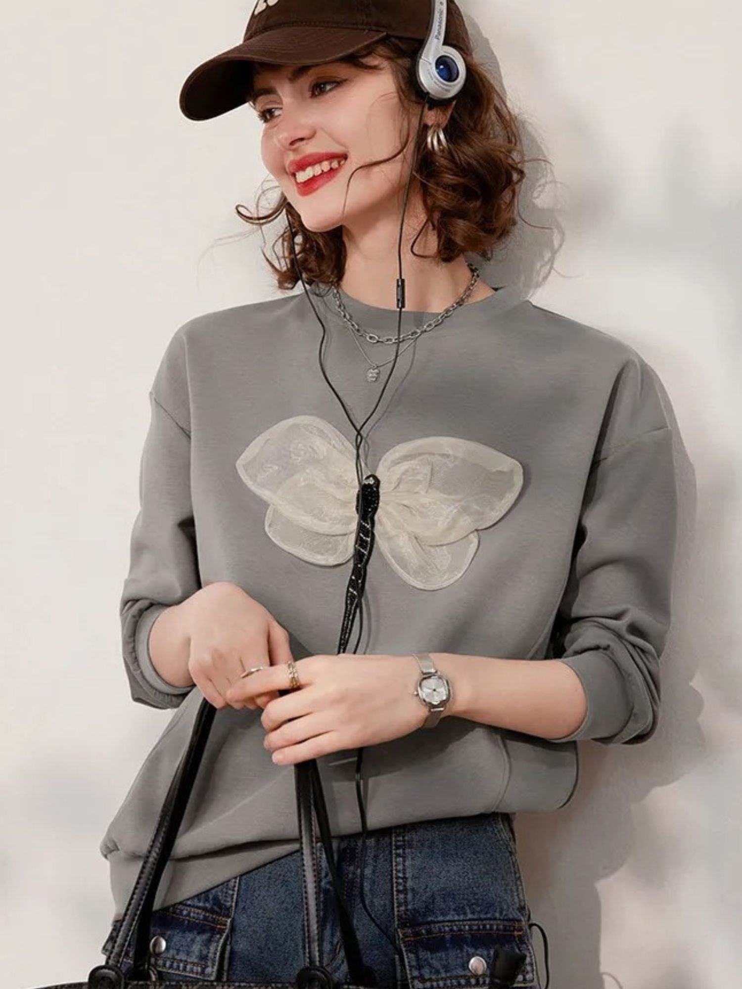 A woman wearing a grey jumper with a 3D dragonfly decoration on the front, paired with denim shorts