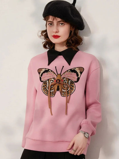 A woman wearing a pink jumper with a butterfly embroidery on the front and a black hat