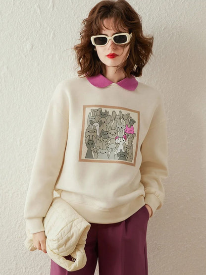Woman wearing an ivory sweatshirt with graphic print, styled with pink collared shirt and skirt, holding a clutch