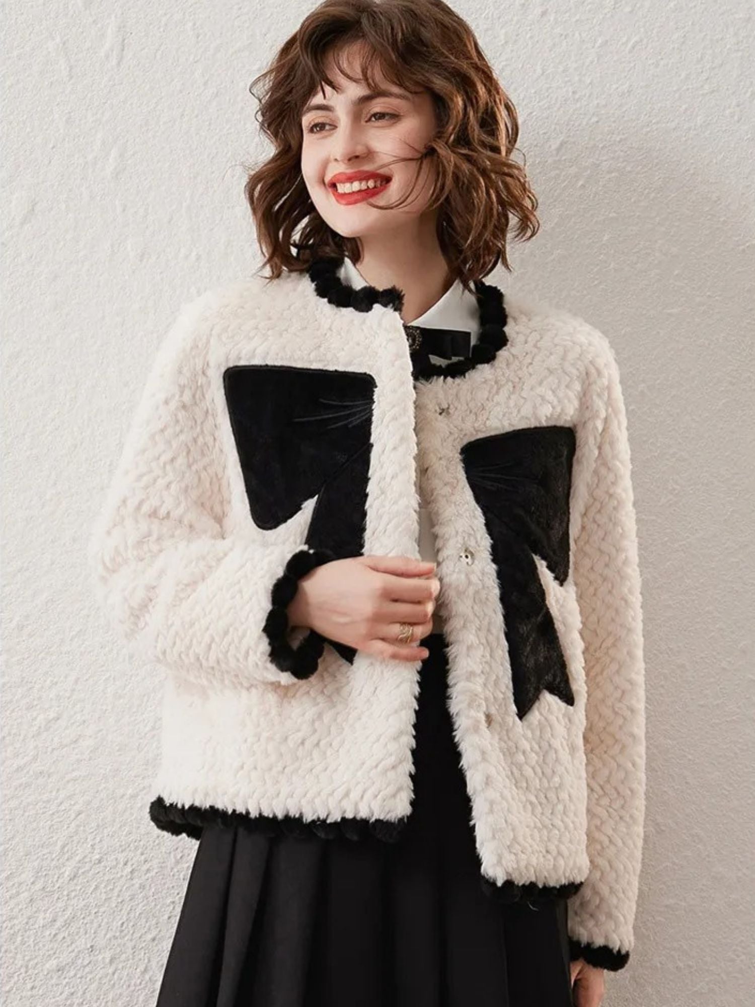 Woman wearing a white textured cardigan with large black bow designs, smiling against a plain background