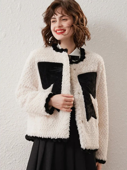 Woman wearing a white textured cardigan with large black bow designs, smiling against a plain background