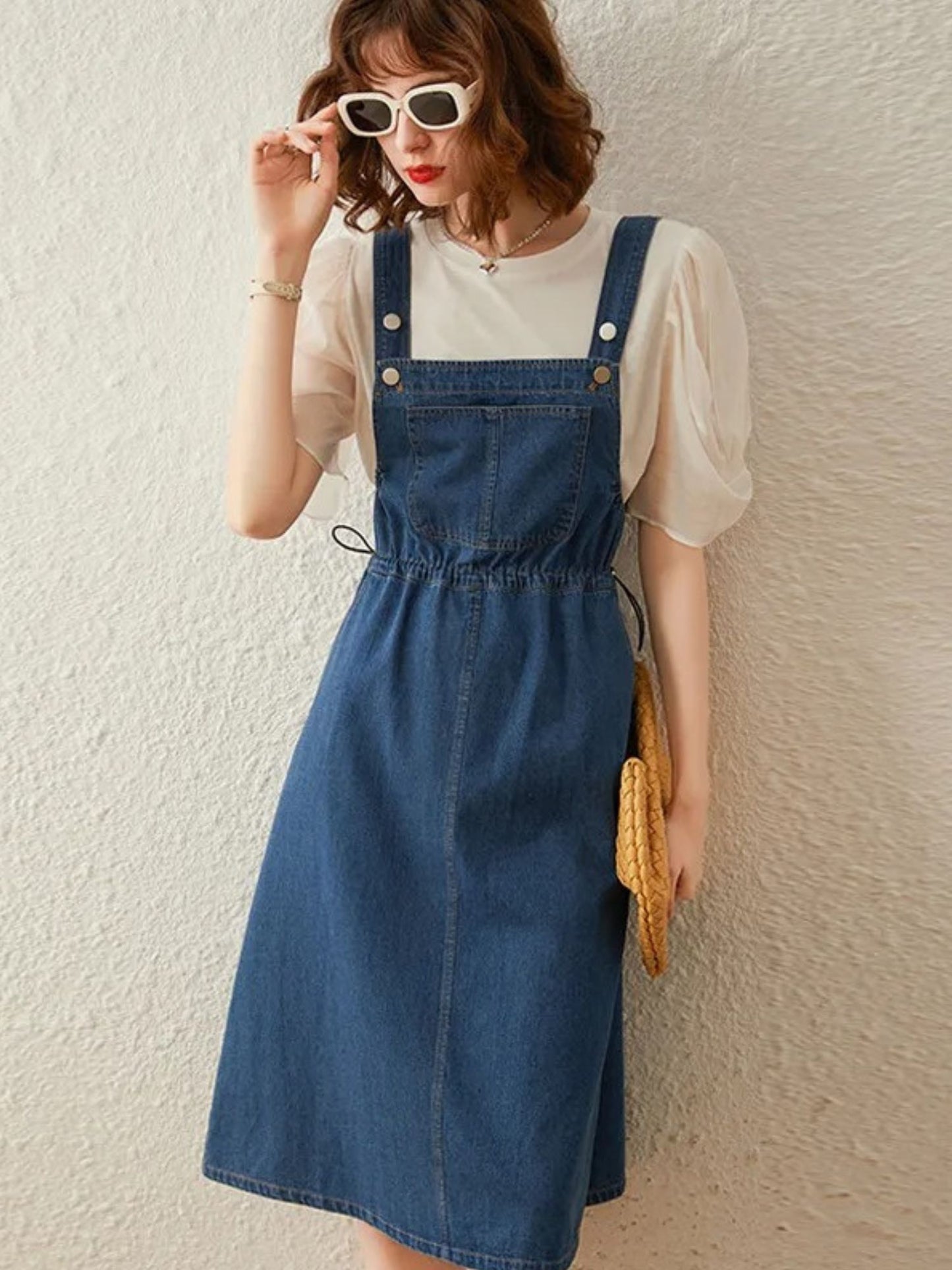 Angled view showing front of denim overall dress with blouse underneath